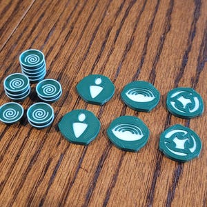 May include: A set of green and white game pieces with different symbols. The pieces are circular and have a raised design. There are also several stacks of smaller green and white circular pieces.