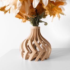 May include: A light brown wooden vase with a geometric design. The vase is made of thin strips of wood that are woven together to create a unique and modern look. The vase is empty and ready to be filled with flowers.