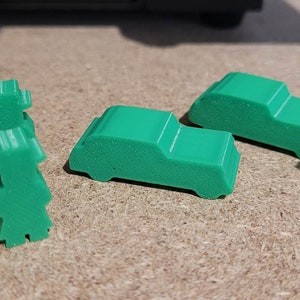 May include: Five green plastic game pieces, including two cars and three people. The pieces are designed for a board game.