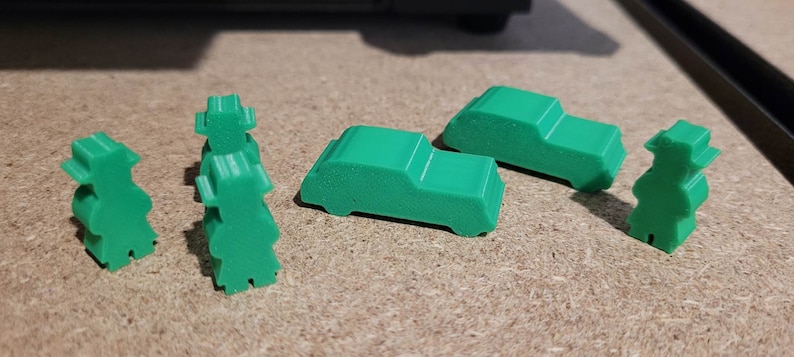 May include: Five green plastic game pieces, including two cars and three people. The pieces are designed for a board game.