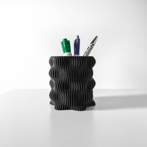 Può includere: Organizzatore da scrivania nero ondulato con un pennarello verde, una penna viola e una penna bianca e nera.