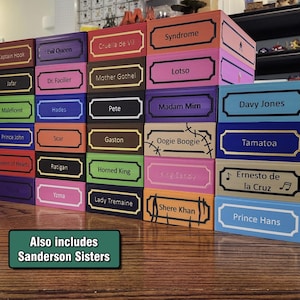 May include: A collection of rectangular boxes in various colors, each featuring a decorative label with a character name printed in black. Names include Captain Hook, Jafar, Maleficent, Prince John, Queen of Hearts, Evil Queen, Dr. Facilier, Hades, Scar, Ratigan, Yzma, Cruella de Vil, Mother Gothel, Pete, Gaston, Horned King, Lady Tremaine, Syndrome, Lotso, Madam Mim, Oogie Boogie, Shere Khan, Davy Jones, Tamatoa, Ernesto de la Cruz, and Prince Hans. A green sign states: Also includes Sanderson Sisters.