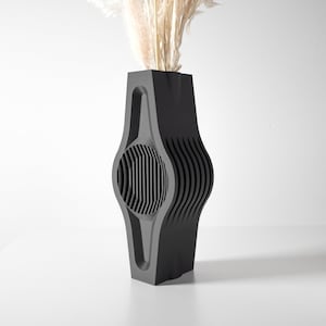 Könnte beinhalten: Eine schwarze Keramikvase mit einem einzigartigen, geometrischen Design. Die Vase hat eine breite, runde Öffnung und einen schmalen Boden. Sie ist aus einem glatten, matten Material gefertigt.