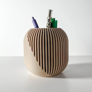 Può includere: Un portaoggetti da scrivania in legno beige con un design unico e a coste. Ha una forma curva e contiene tre penne.