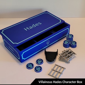 May include: A blue box with a drawer and the word "Hades" on the top. The box is open and contains a variety of game pieces, including a black skull, grey bars, and blue tokens with a skull symbol.
