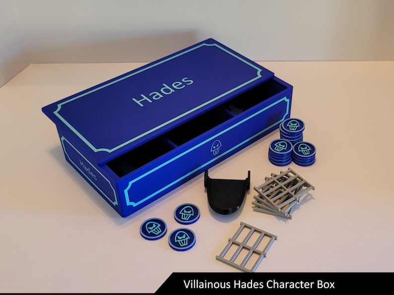 May include: A blue box with a drawer and the word "Hades" on the top. The box is open and contains a variety of game pieces, including a black skull, grey bars, and blue tokens with a skull symbol.