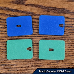 May include: Four blank counter dial cases, two blue and two green, with a small rectangular cutout in the centre of each.  Blank Counter X Dial Cases.