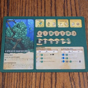 Könnte beinhalten: Eine grüne Spielkarte mit dem Titel "A Spread of Rampant Green". Die Karte zeigt eine grüne Kreatur mit einem großen Auge und einem grünen Hintergrund. Die Karte hat einen Wachstumsbereich, einen Bereich für Plus-Pick-One und einen Bereich für private Kräfte. Der Bereich für private Kräfte enthält den Text "Creepers Tear Into Mortar" und "All Enveloping Green".