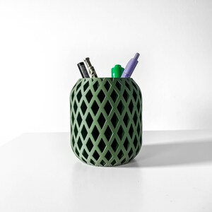 Può includere: Un portapenne verde con un motivo a rombi e tre penne al suo interno. Il portapenne è realizzato in plastica testurizzata.