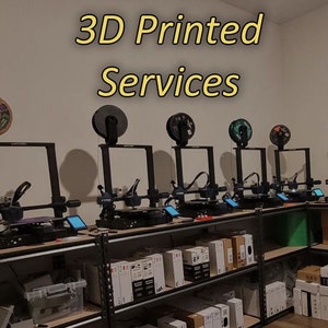 May include: A row of black 3D printers on a metal shelf with a sign that reads "3D Printed Services".