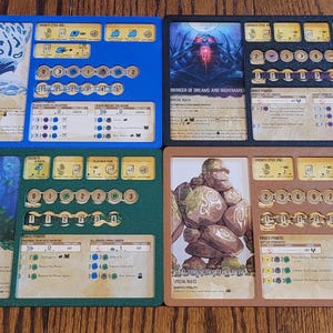 May include: Four game board components with illustrations and text. The boards are blue, green, black, and brown. Each board has slots for tokens and cards. The illustrations depict fantasy creatures and landscapes.