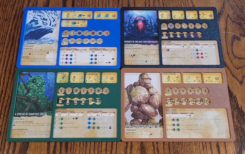 May include: Four game board components with illustrations and text. The boards are blue, green, black, and brown. Each board has slots for tokens and cards. The illustrations depict fantasy creatures and landscapes.