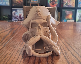 May include: A 3D printed skull wearing a pirate hat and a tentacle beard. The skull has a crossbones design on the hat and is made of a light brown plastic.