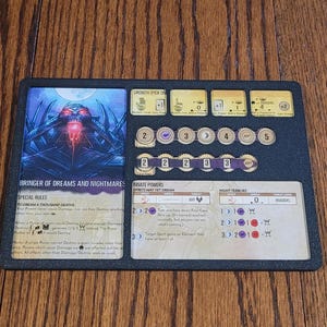 May include: A black and gold board game component with a fantasy illustration of a creature with glowing red eyes. The text "Bringer of Dreams and Nightmares" is printed on the card. The card also includes special rules, innate powers, and night terrors.