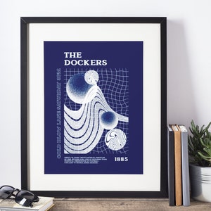 Può includere: Una stampa artistica incorniciata con sfondo blu navy presenta il testo "THE DOCKERS" e "COLD BLOW LANE SATURDAY 3PM". Sono presenti anche forme astratte bianche e un motivo a griglia. La stampa è esposta su una superficie di legno.