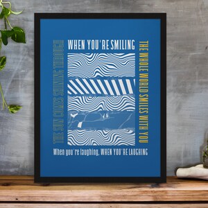 Puede incluir: Una impresión artística enmarcada con fondo azul y texto blanco. El texto dice "When You're Smiling" y "The Whole World Smiles With You". La impresión también presenta patrones de ondas abstractas y la frase "The Sun Comes Shining Through."