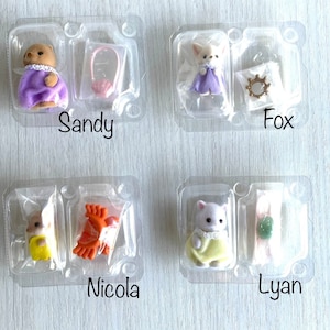 Peut inclure: Quatre figurines miniatures d'animaux dans un emballage plastique transparent. Chaque figurine porte une robe ou une tenue. Les noms "Sandy", "Fox", "Nicola" et "Lyan" sont imprimés sous chaque emballage. Accessoires : sac à main, gants et gemme.