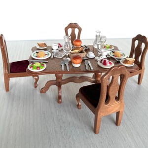 Puede incluir: Un juego de mesa de comedor de madera en miniatura con cuatro sillas, una tapa de mesa marrón y un asiento de terciopelo rojo en cada silla. La mesa está puesta con platos, cubiertos y alimentos en miniatura.