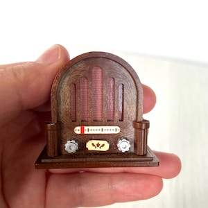 May include: A miniature wooden radio with a brown finish and a red and white dial. The radio has a decorative design with a floral motif on the front.