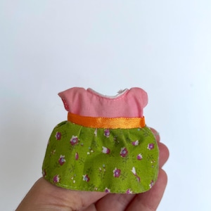 May include: A pink and green doll dress with a floral print and an orange ribbon.