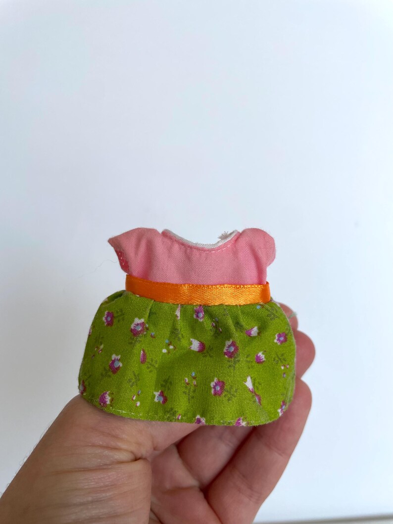 May include: A pink and green doll dress with a floral print and an orange ribbon.