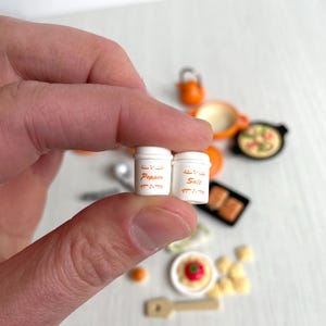 May include: Two miniature white salt and pepper shakers with orange lettering. The shakers say "Salt" and "Pepper" on them.