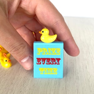 Op de afbeelding: Een blauw en geel bord met de tekst "PRIZE EVERY TIME" en een gele rubberen eend erop.
