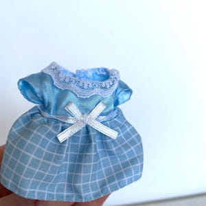 May include: A light blue dress with a white lace collar and a white bow. The dress has a checkered pattern.