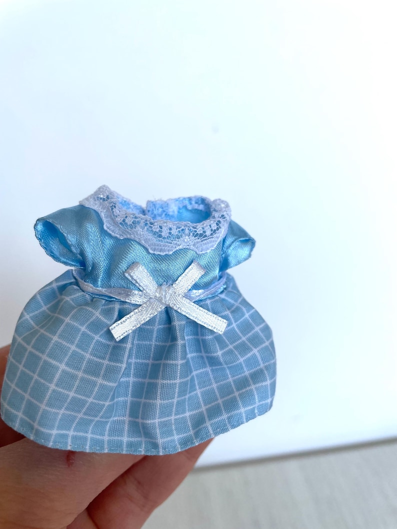 May include: A light blue dress with a white lace collar and a white bow. The dress has a checkered pattern.