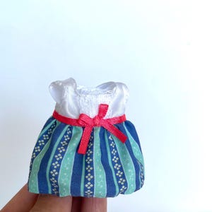 May include: A miniature blue and green striped dress with a white bodice and a red ribbon bow.