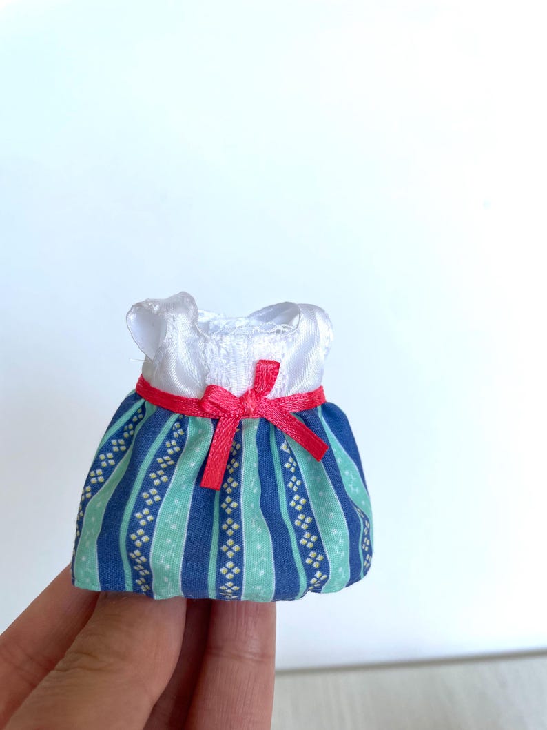 May include: A miniature blue and green striped dress with a white bodice and a red ribbon bow.