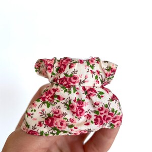 May include: A small, white dress with a pink and green floral print. The dress has a ruffled neckline and short sleeves.