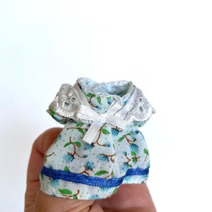 May include: A miniature blue and white floral dress with a white lace collar and blue ribbon bow. The dress has a blue ribbon trim around the bottom.