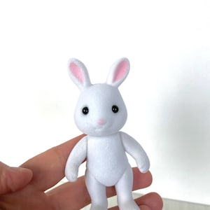 May include: A white plush rabbit toy with pink ears and black eyes. The rabbit is standing on its hind legs with its front paws outstretched.
