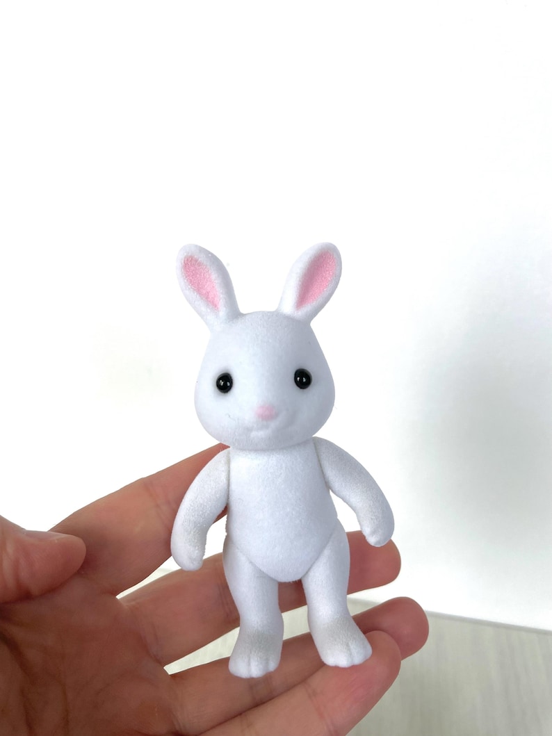 May include: A white plush rabbit toy with pink ears and black eyes. The rabbit is standing on its hind legs with its front paws outstretched.
