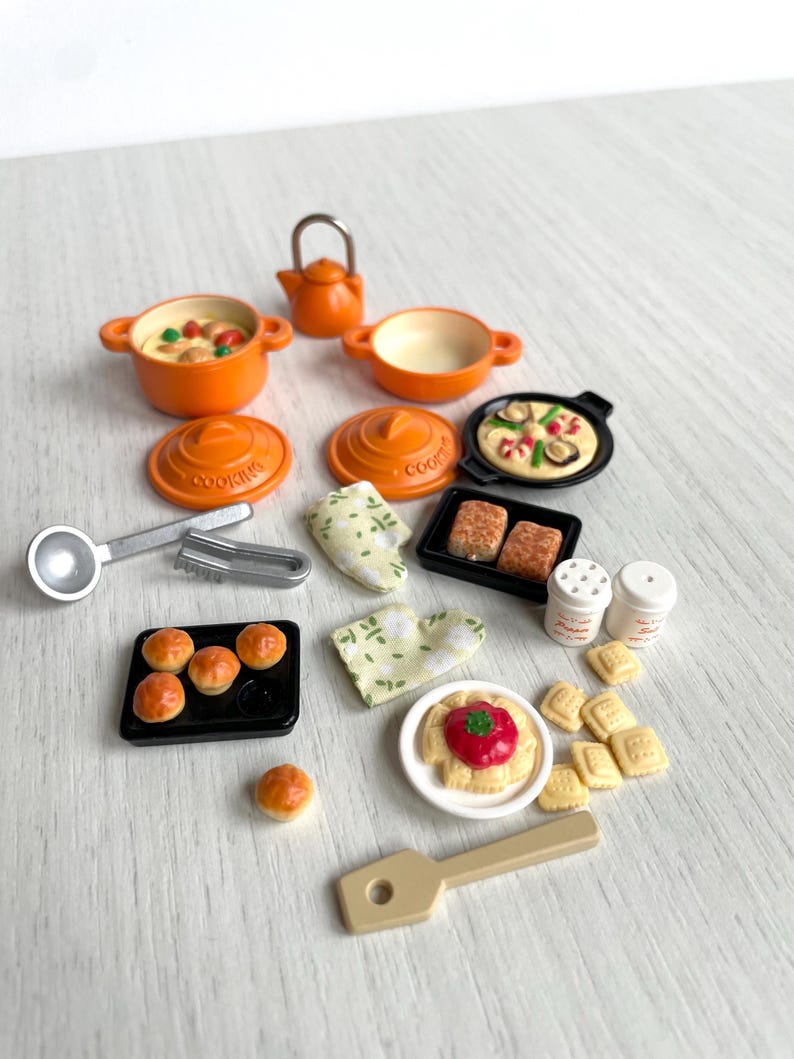 May include: A miniature kitchen playset with orange pots, pans, and a teapot. There are also miniature food items, including pizza, bread, and pastries. The set includes a spatula, tongs, and two salt and pepper shakers.