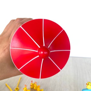 Op de afbeelding: Een rode en witte plastic speelgoedparaplu met een geel rubberen eendjespel. De eendjes staan in een rij op een houten oppervlak.