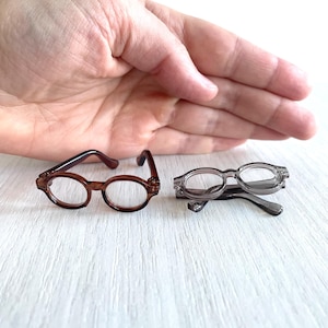 Puede incluir: Dos pares de gafas pequeñas y redondas. Un par es marrón y el otro es gris.