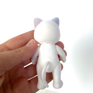 May include: White plush cat toy with purple ears. The cat is standing on its hind legs with its tail curled behind it.