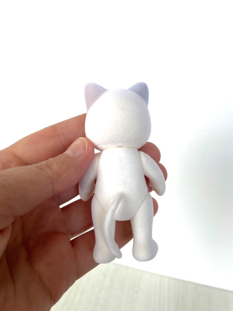 May include: White plush cat toy with purple ears. The cat is standing on its hind legs with its tail curled behind it.