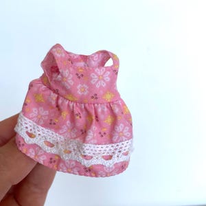 May include: A pink sleeveless dress with a white lace trim and a floral pattern.