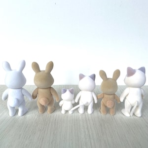 May include: Five small plush toys, including two white bunnies, two brown bunnies, and a white cat, all facing away from the camera. The toys are arranged in a line on a light brown wooden surface.
