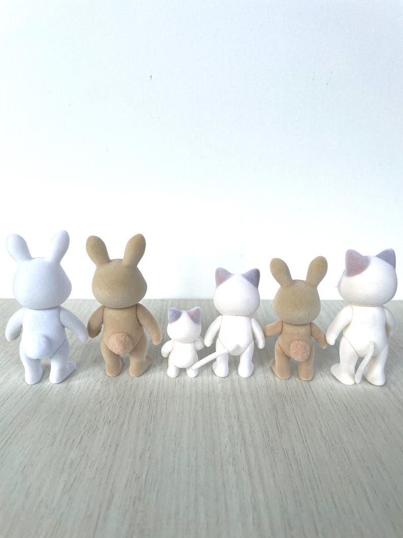 May include: Five small plush toys, including two white bunnies, two brown bunnies, and a white cat, all facing away from the camera. The toys are arranged in a line on a light brown wooden surface.