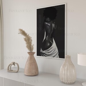 May include: A black and white illustration of a person with their back to the viewer, standing in a white cloth. The illustration is framed and hanging on a white wall.