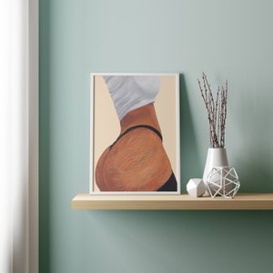 May include: A framed painting of a woman's back with a white shirt and black underwear. The painting is on a light brown shelf with a white vase and a white decorative object.