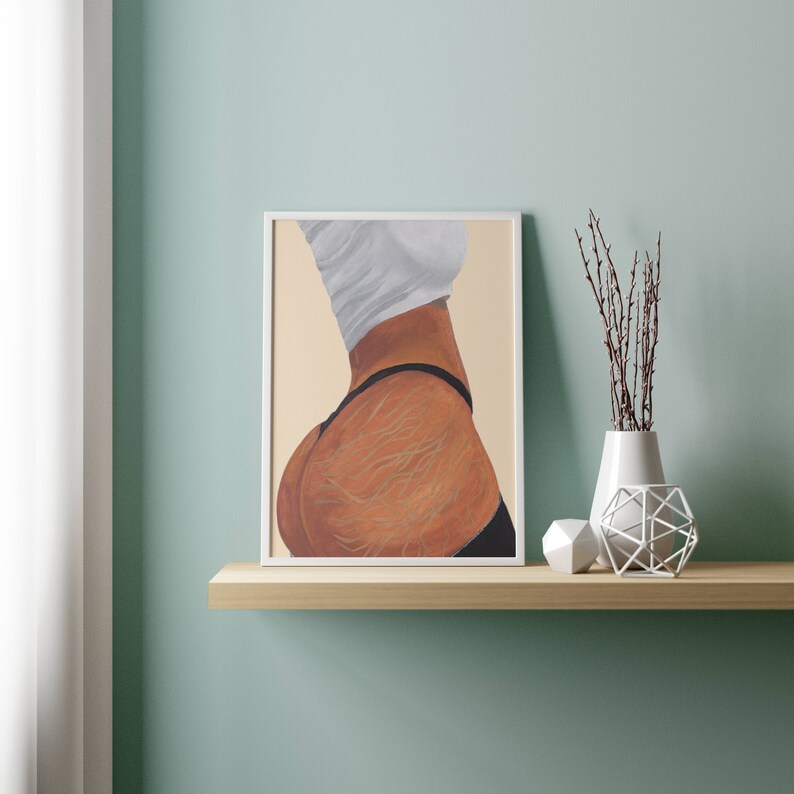 May include: A framed painting of a woman's back with a white shirt and black underwear. The painting is on a light brown shelf with a white vase and a white decorative object.