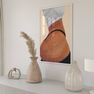 May include: A framed print of a painting depicting a woman's back with visible stretch marks. The painting is in a white frame and is hanging on a white wall.
