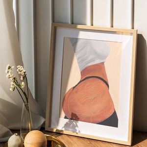 May include: A framed illustration of a person's back with detailed lines drawn on the skin. The illustration is in a light brown wooden frame and is sitting on a wooden floor.