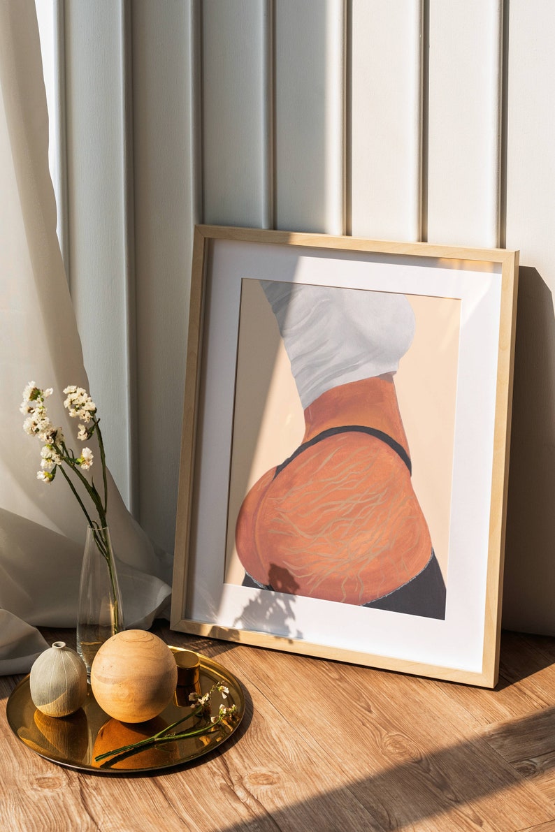 May include: A framed illustration of a person's back with detailed lines drawn on the skin. The illustration is in a light brown wooden frame and is sitting on a wooden floor.