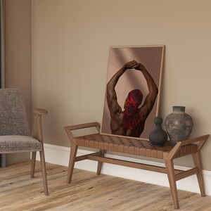 Puede incluir: Una impresi&oacute;n enmarcada de una persona de espaldas, con un pa&ntilde;uelo rojo en la cabeza, con los brazos levantados por encima de la cabeza. La impresi&oacute;n est&aacute; colgada en una pared sobre un banco de madera con un asiento tejido.
